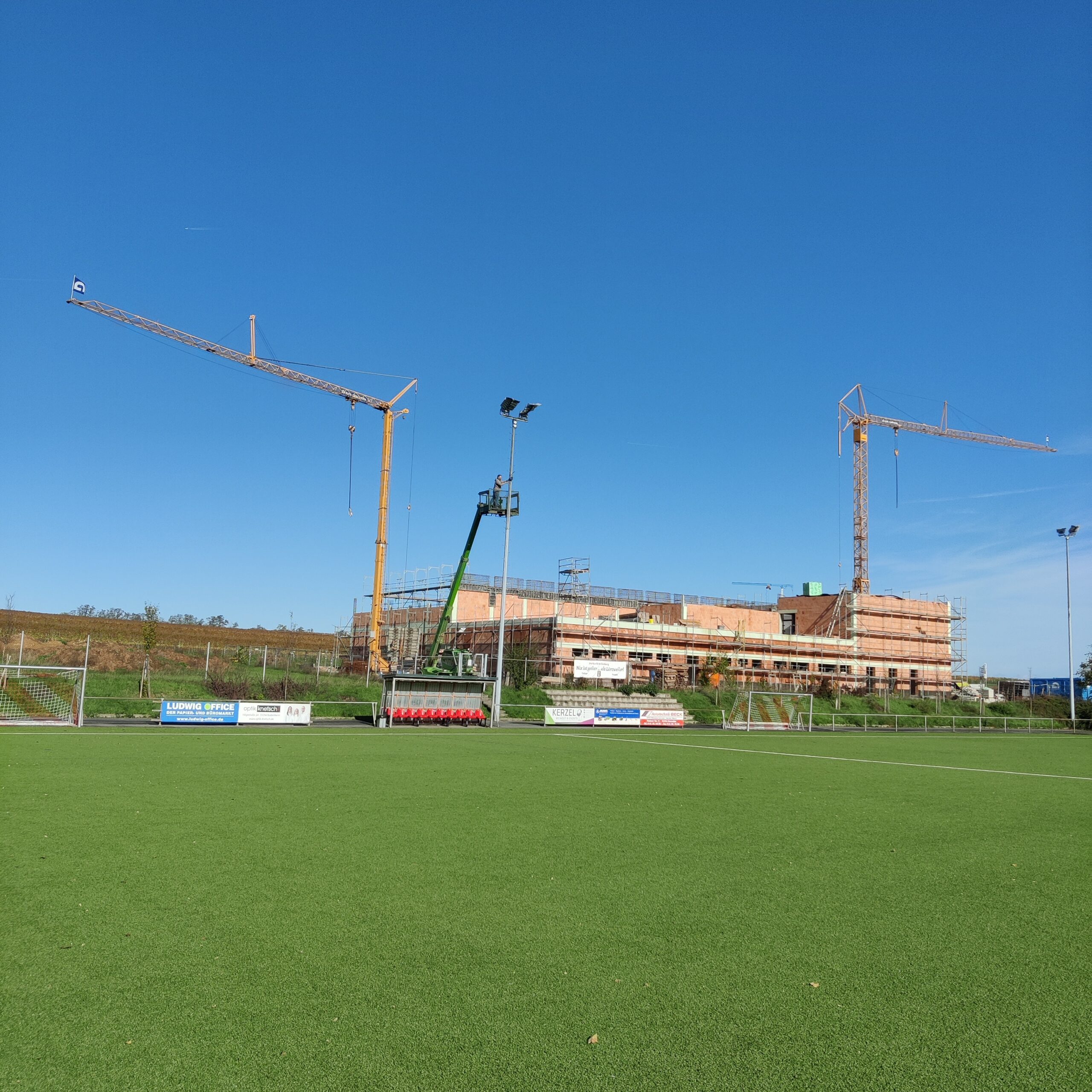 Blick auf die Halle vom Sportplatz aus - im Vordergrund zu sehen der Steiger von Heribert Breivogel mit Korb zur Reparatur der Baucam