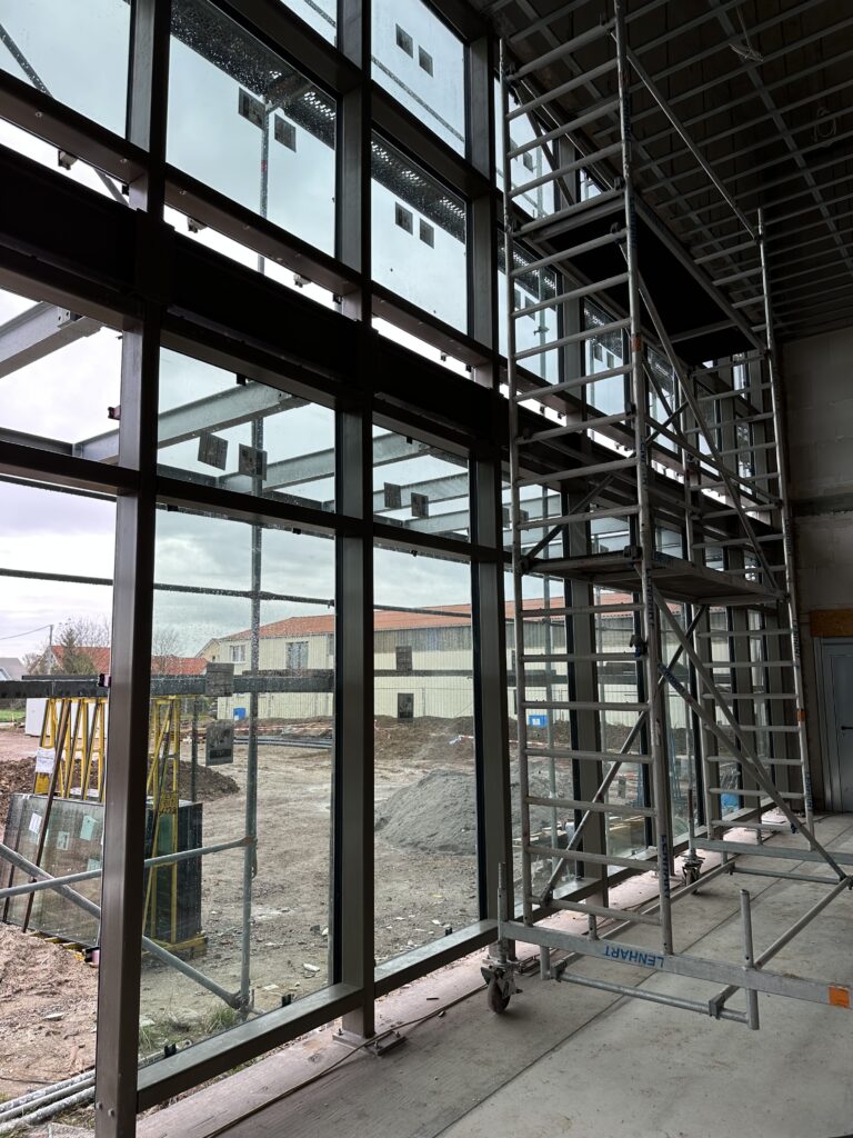 Die Glaswand des Foyer von Innen gesehen. man sieht die dunklen Rahmen der Fenster und die bereits teilweise eingesetzten Scheiben.