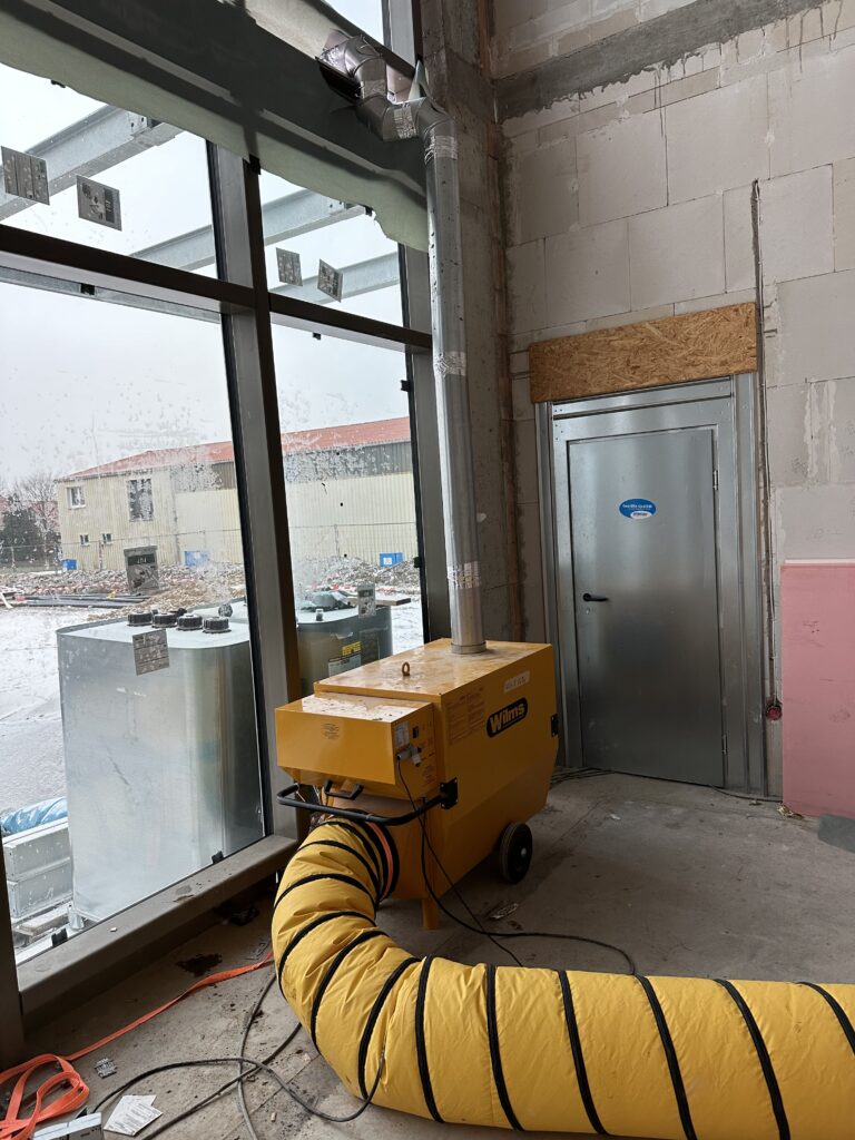 Die Baustellenheizung, ein gelber Kasten auf Rädern, angeschlossen ein ca 40 cm hoher gelber Luftschlauch.