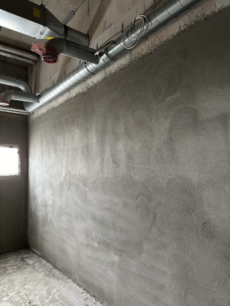 Eine fertig verputzte Wand in einem Raum, darüber Teile der Lüftung.