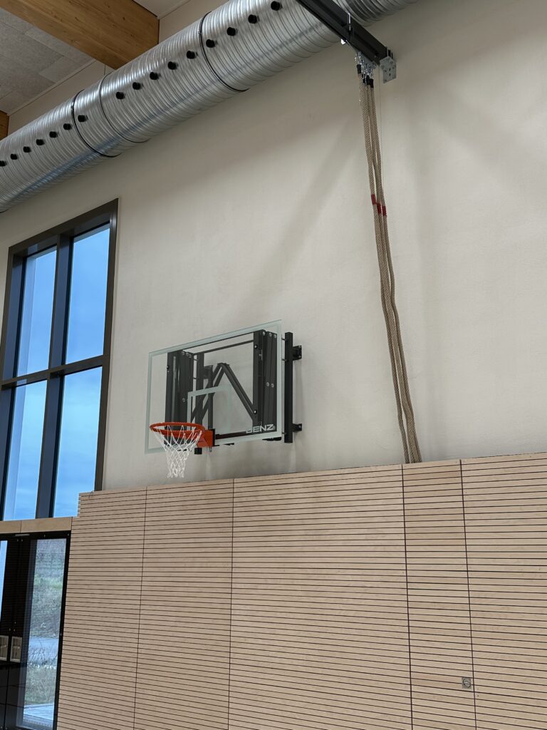 Turnseile hängen an einem grauen Deckenträger, daneben hängt ein Basketballkorb an der Wand, man erkennt, dass man ihn noch von der Wand ausfahren kann.